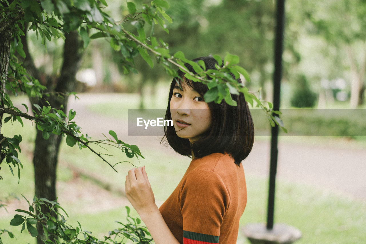 Portrait of young woman standing by plants in park