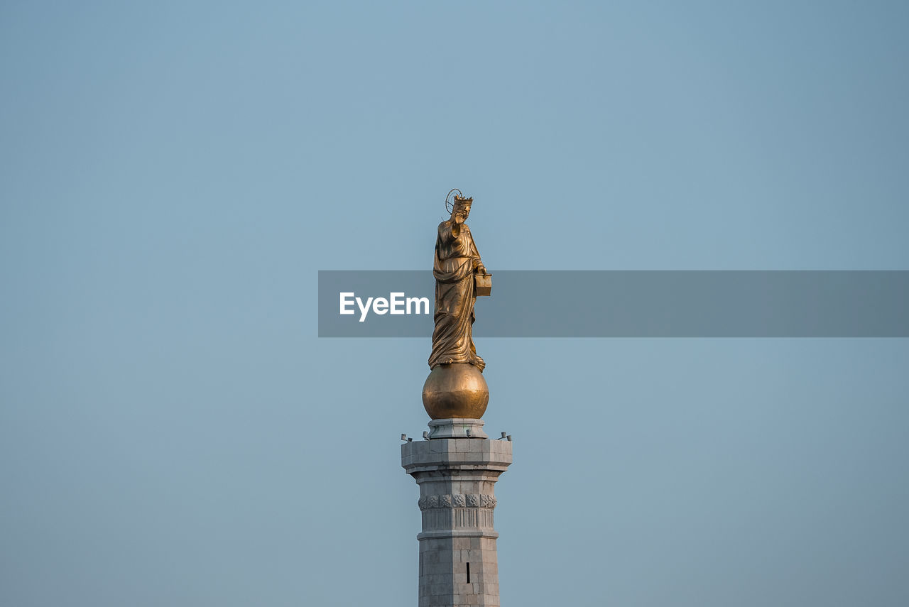 Low angle view of beautiful statue of golden madonna with blue sky in background