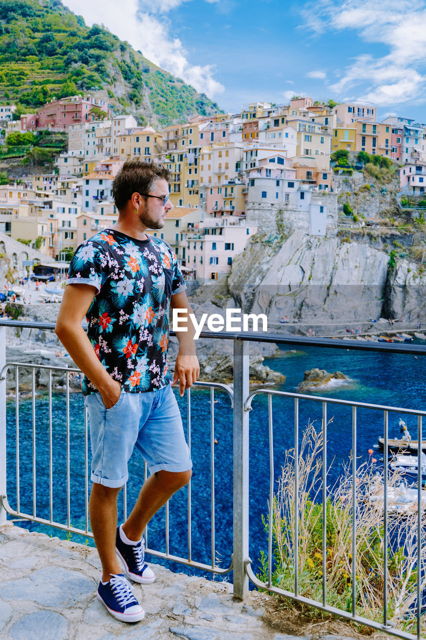 FULL LENGTH OF MAN STANDING BY RAILING AGAINST BUILDINGS