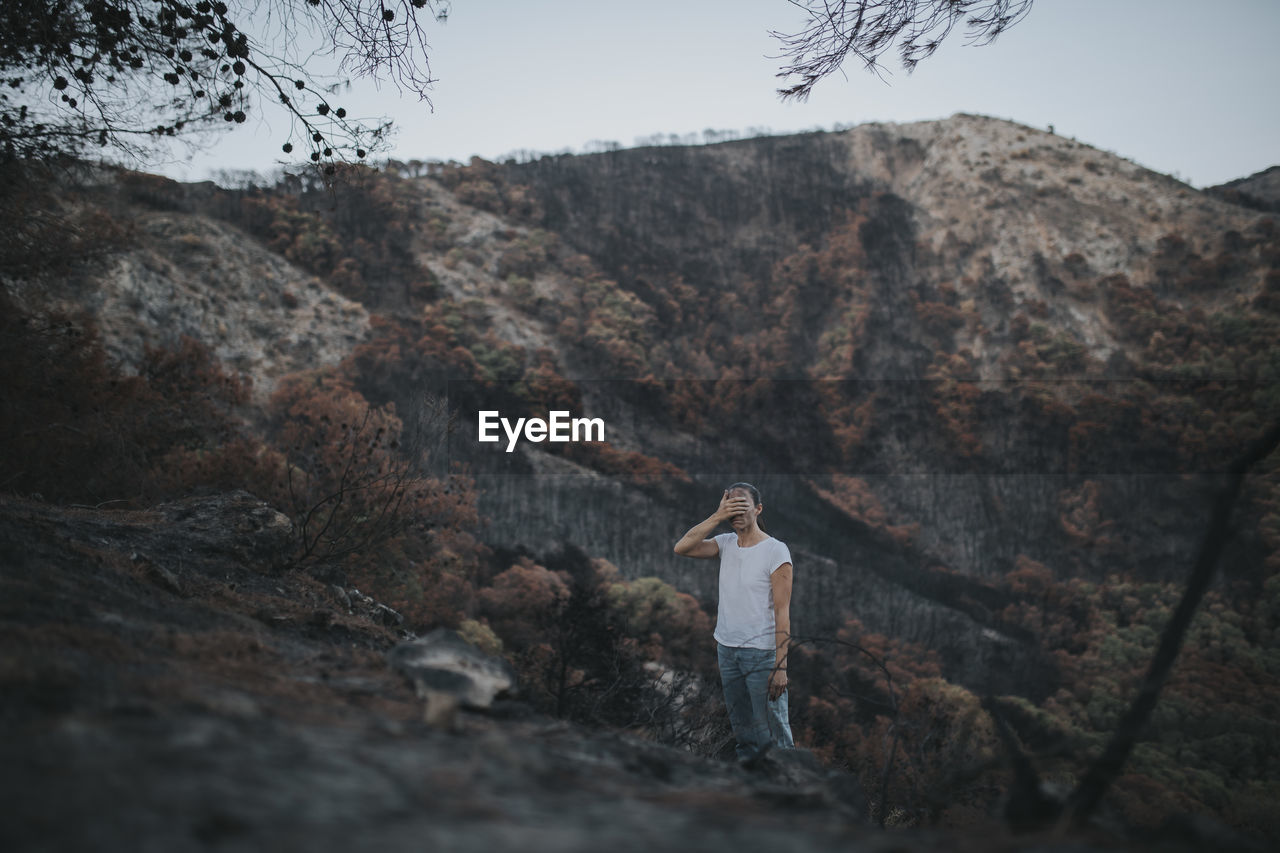 Desperate woman covering face standing in forest