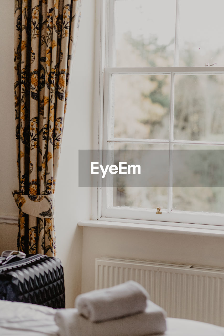 Suitcase placed near window decorated with floral curtain in light hotel room