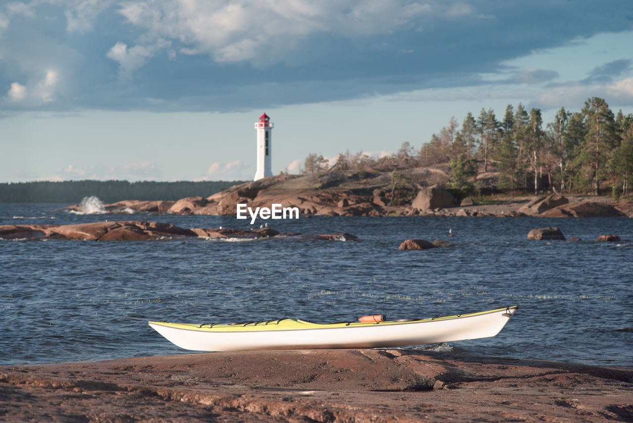 Sea kayak on a rocky shore. lighthouse in background