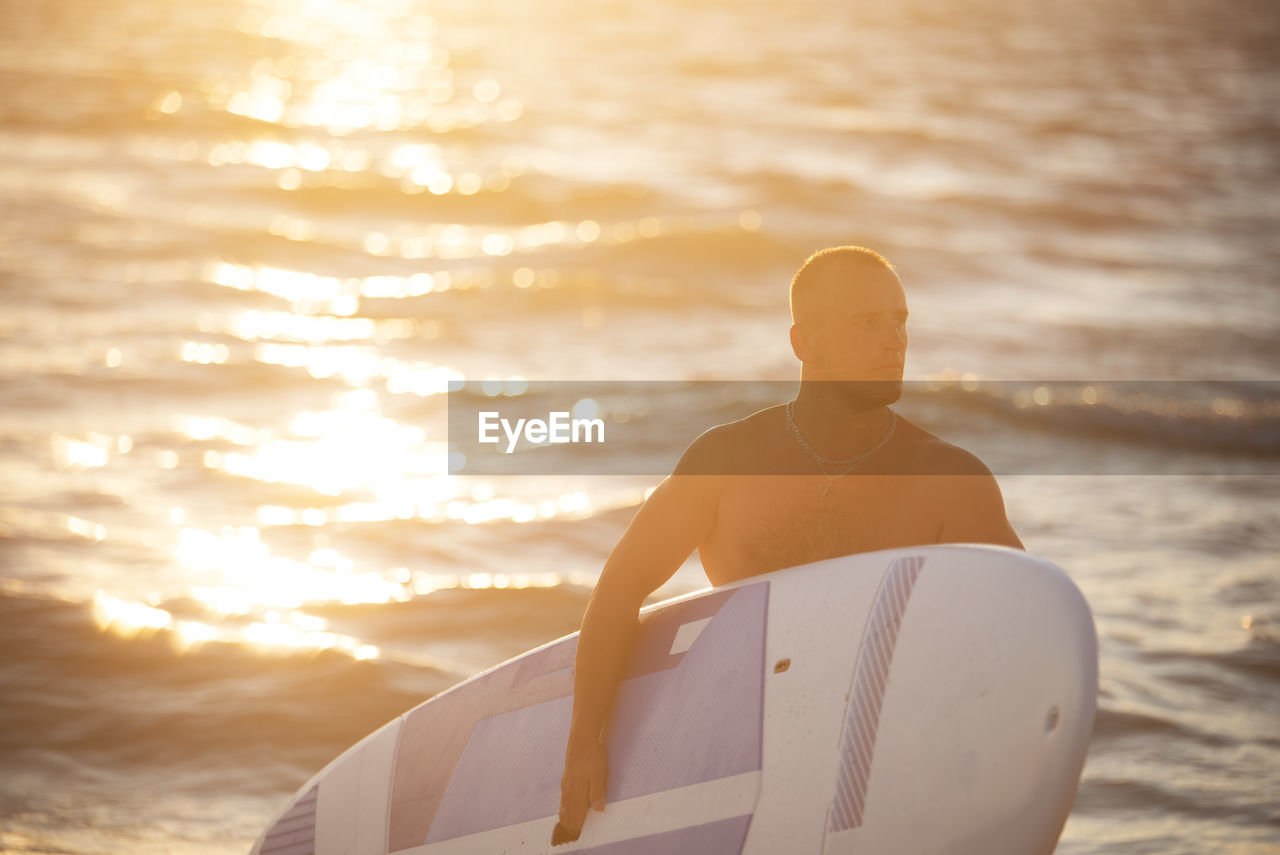 Shirtless muscular young man with surfboard in sea