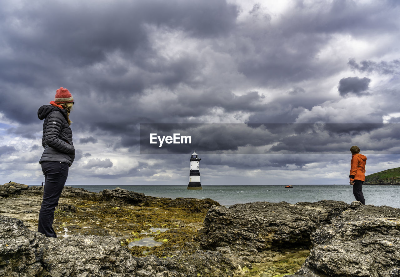 People standing on rock by sea against sky