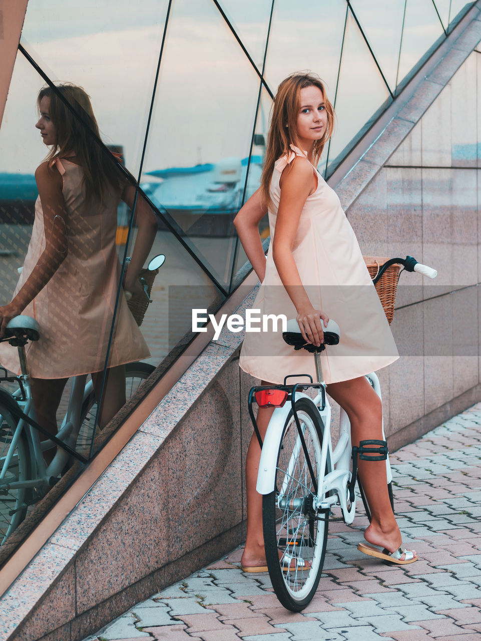 Full length portrait of beautiful woman with bicycle by modern building
