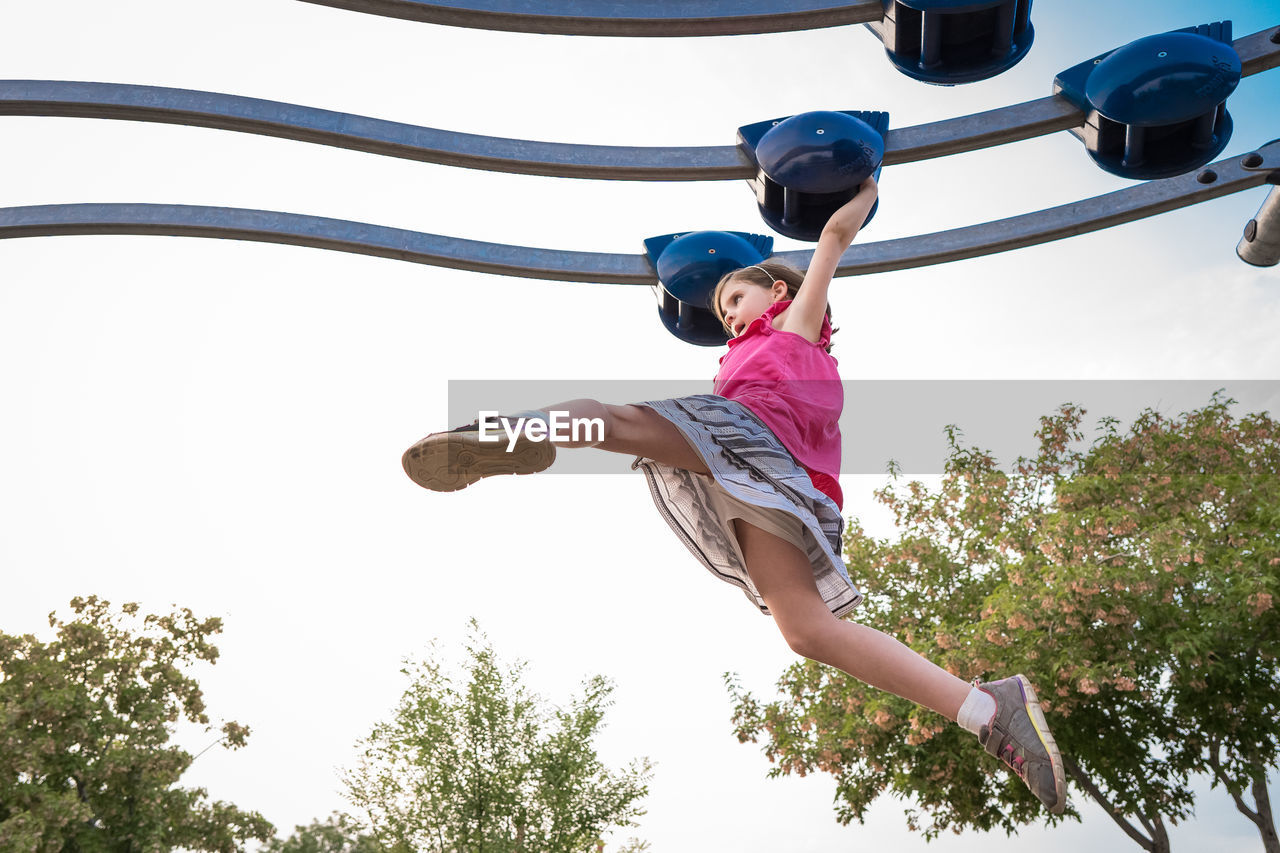 Young girl concentrates swinging her legs on a playground structure