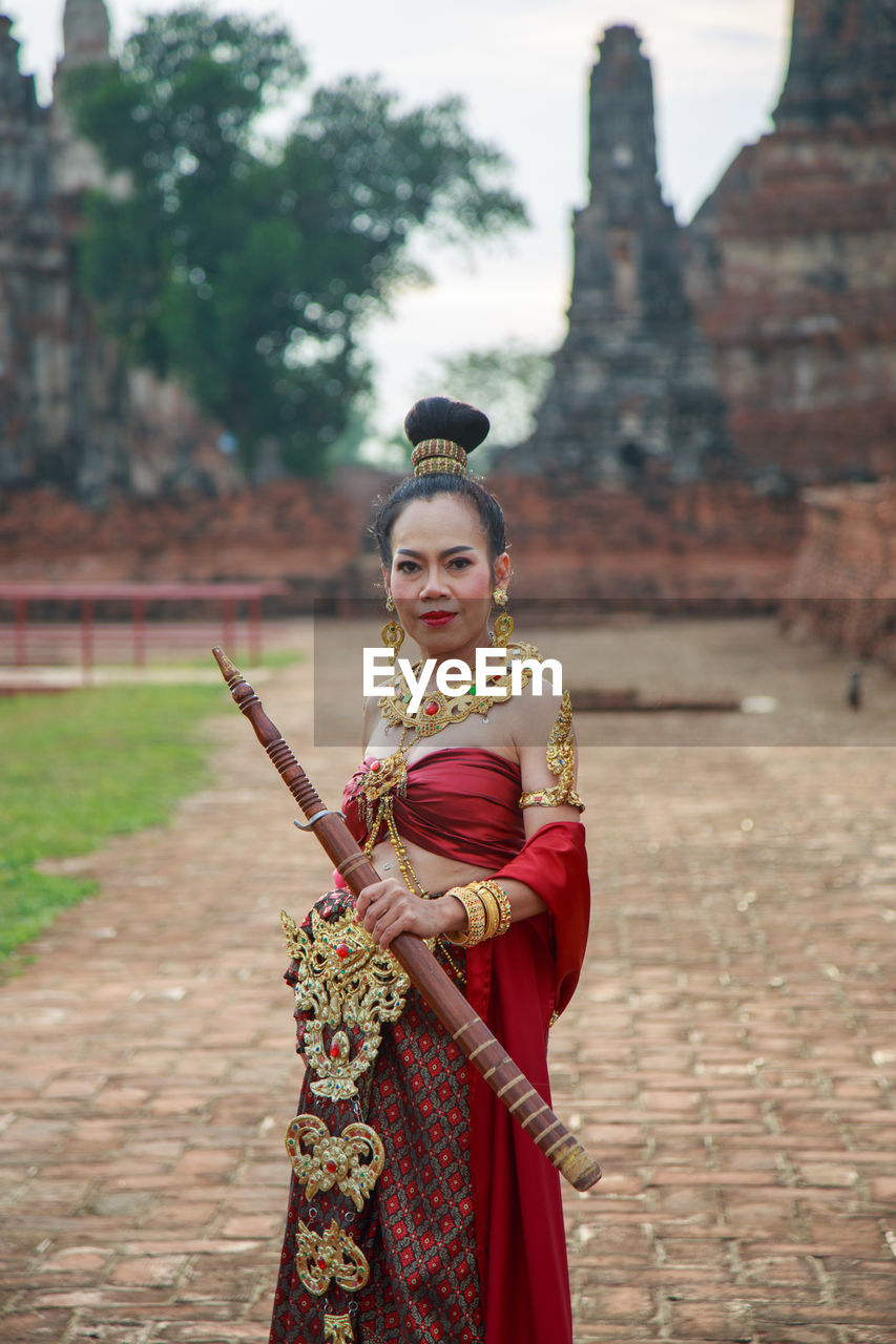 An asian woman in a red thai traditional dress holding an old sword at an ancient ruin temple