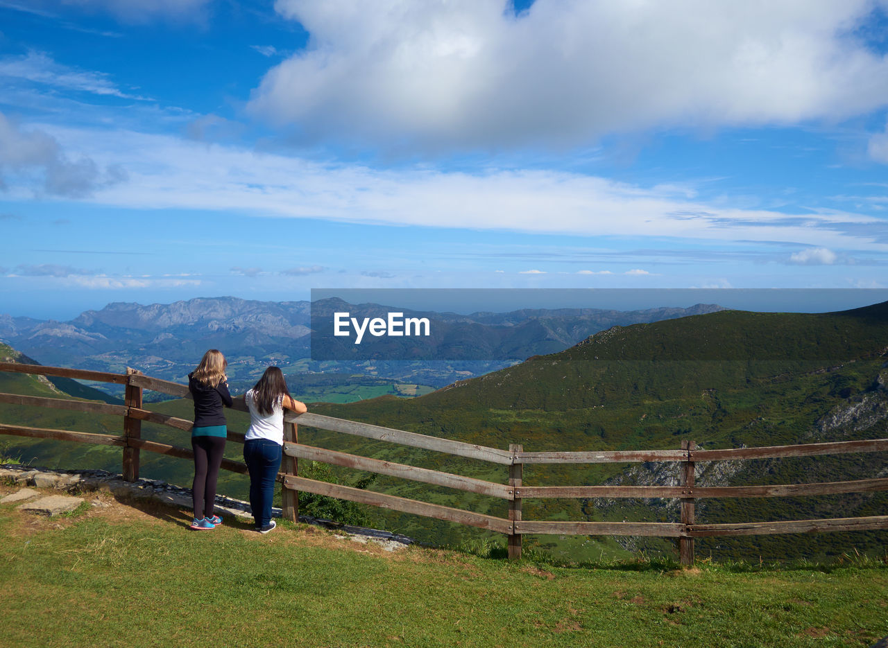 Rear view of women standing by railing against mountains and sky