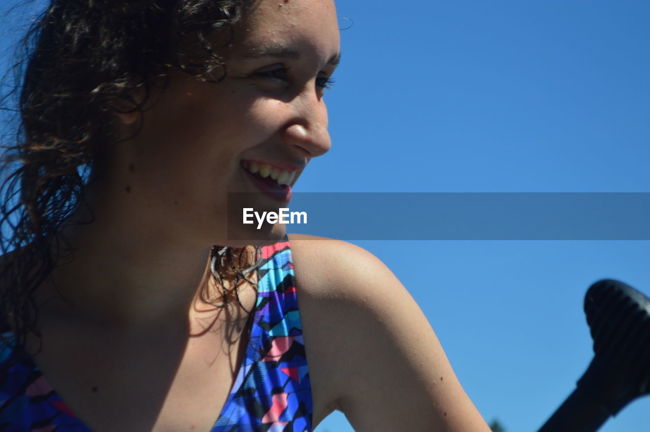 Close-up of smiling teenage girl against clear blue sky