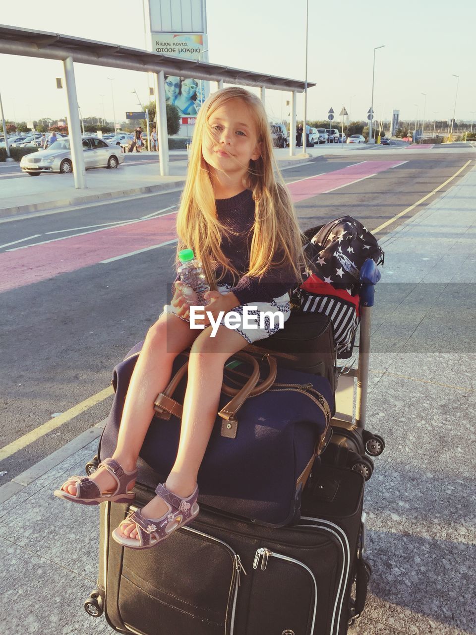 Portrait of smiling girl holding water bottle while sitting on luggage bags