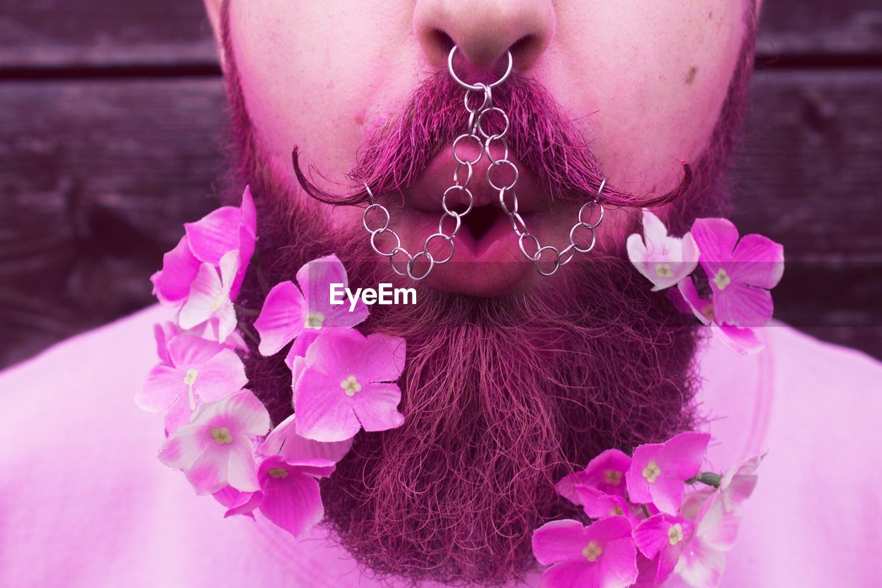 Close-up of pierced man with pink flowers on beard