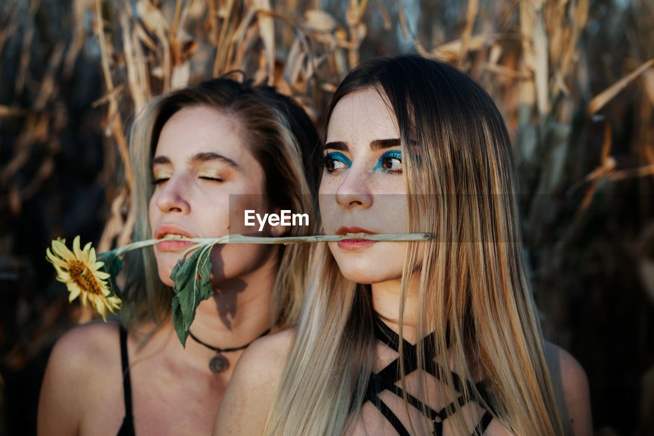 Close-up of beautiful women biting flower while standing against plants