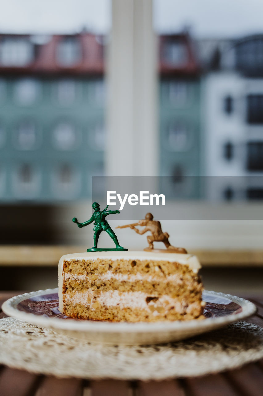 Two toy soldiers fighting on the top of a piece of cake - close up window in background