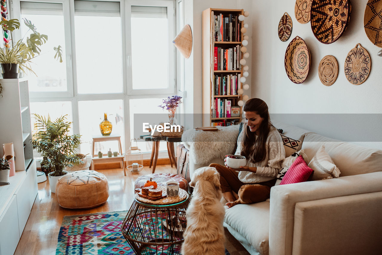 Woman holding food while playing with dog at home