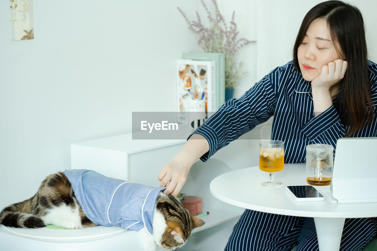 Woman in pajamas cloth drink tea and play with her cat