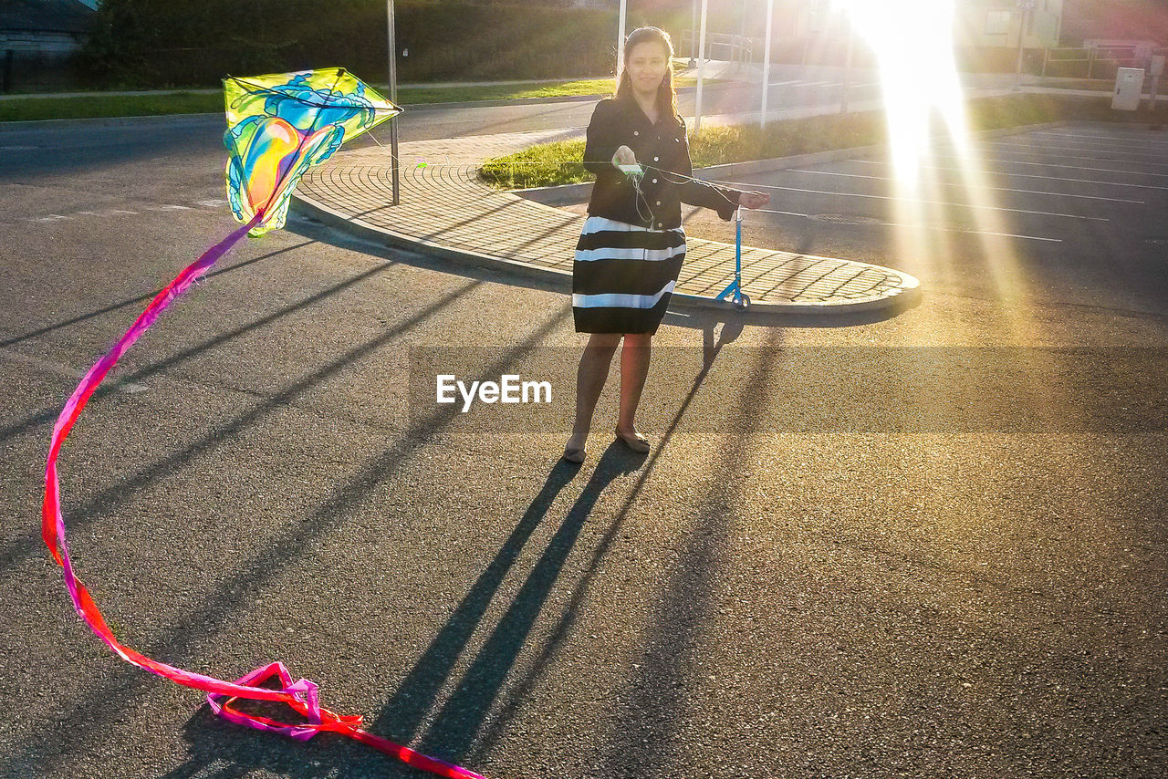 Full length of woman flying kite on road during sunny day