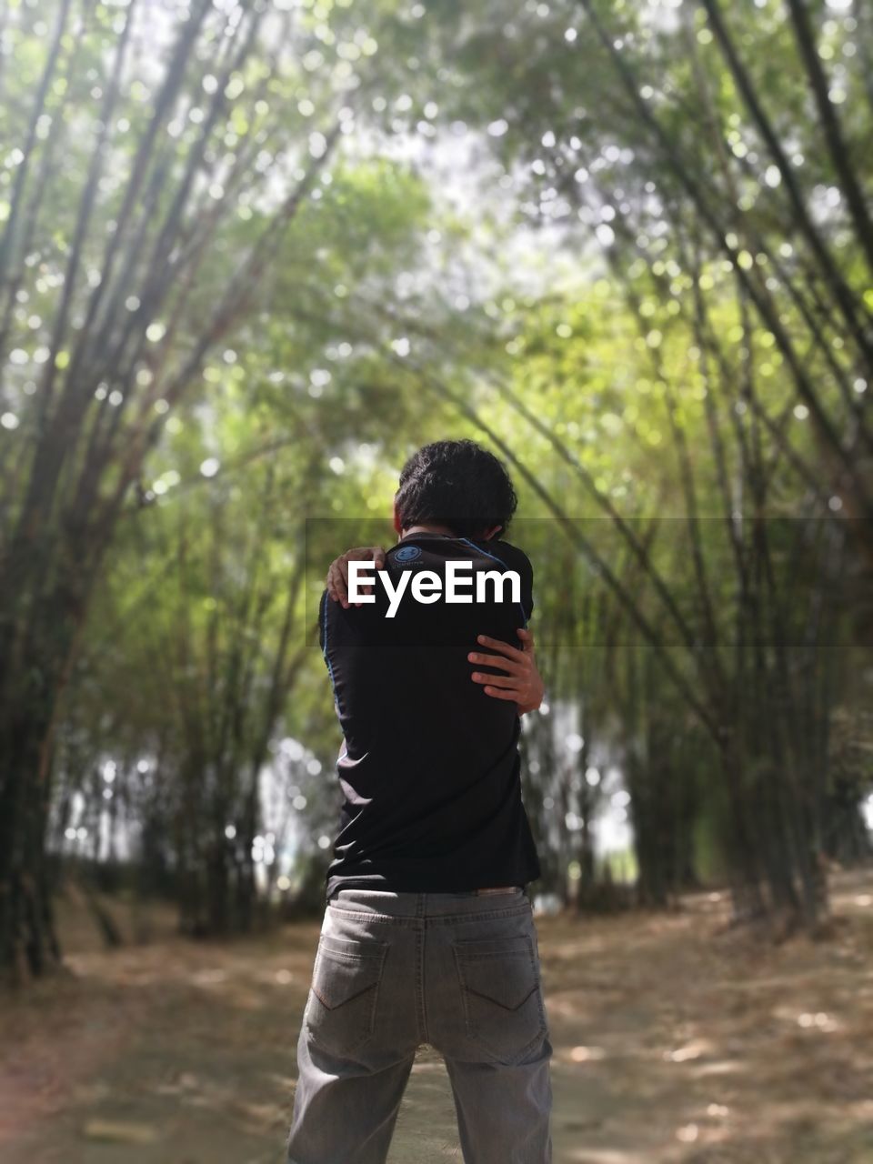 Rear view of man hugging self while standing in forest