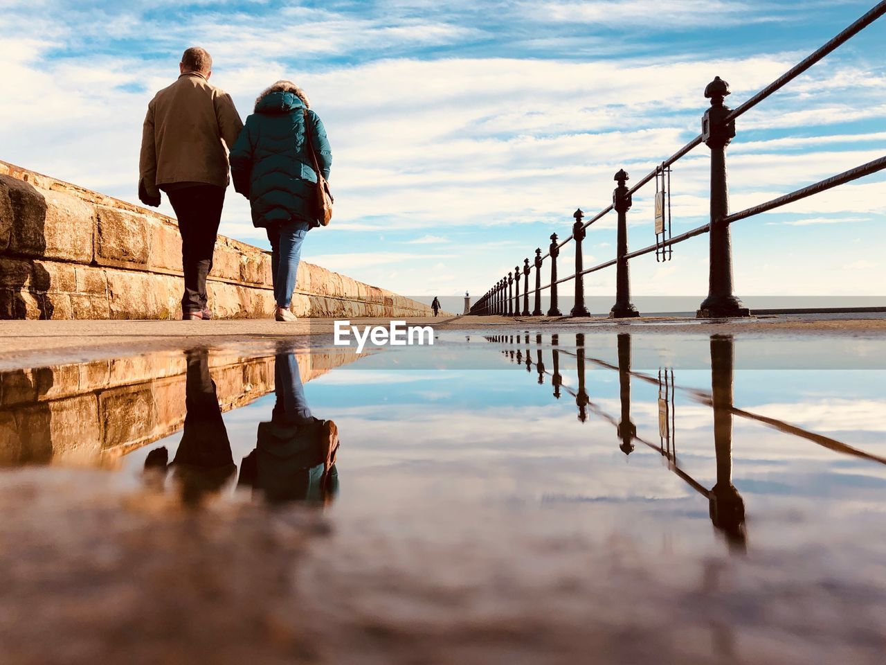 People walking on road with reflection against sky