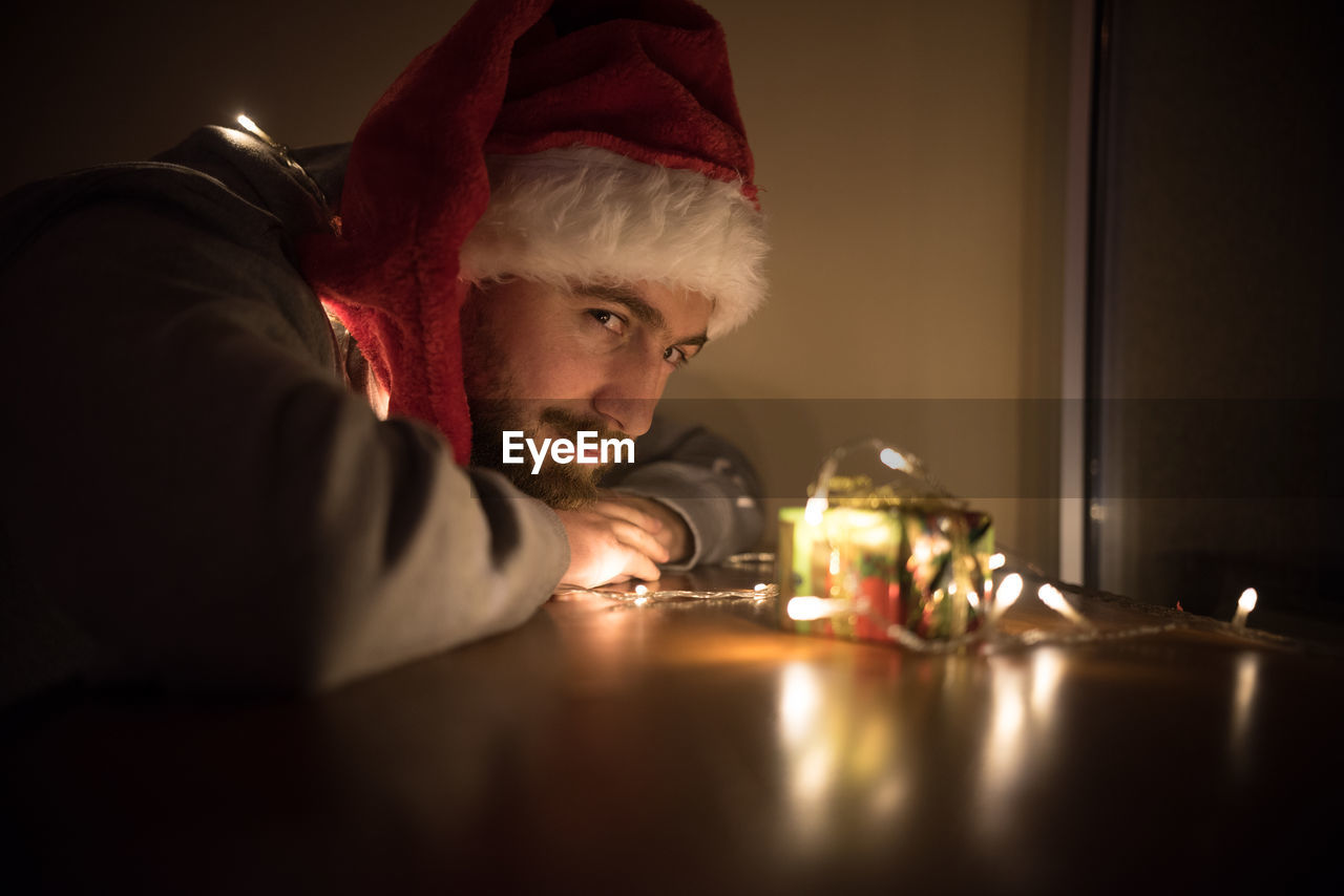 Close-up of young man by illuminated christmas lights on gift in darkroom