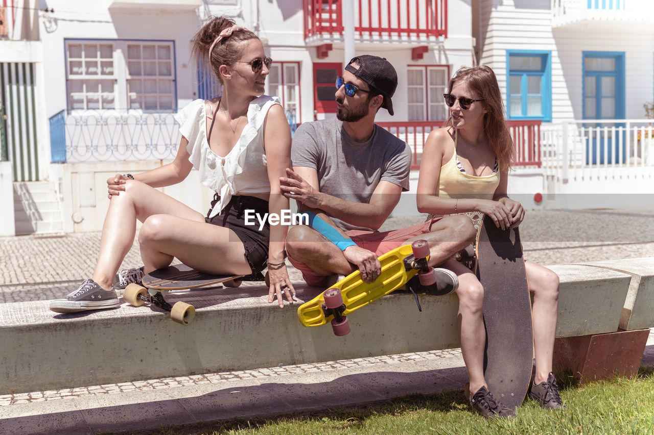 portrait of smiling friends using digital tablet while sitting on street