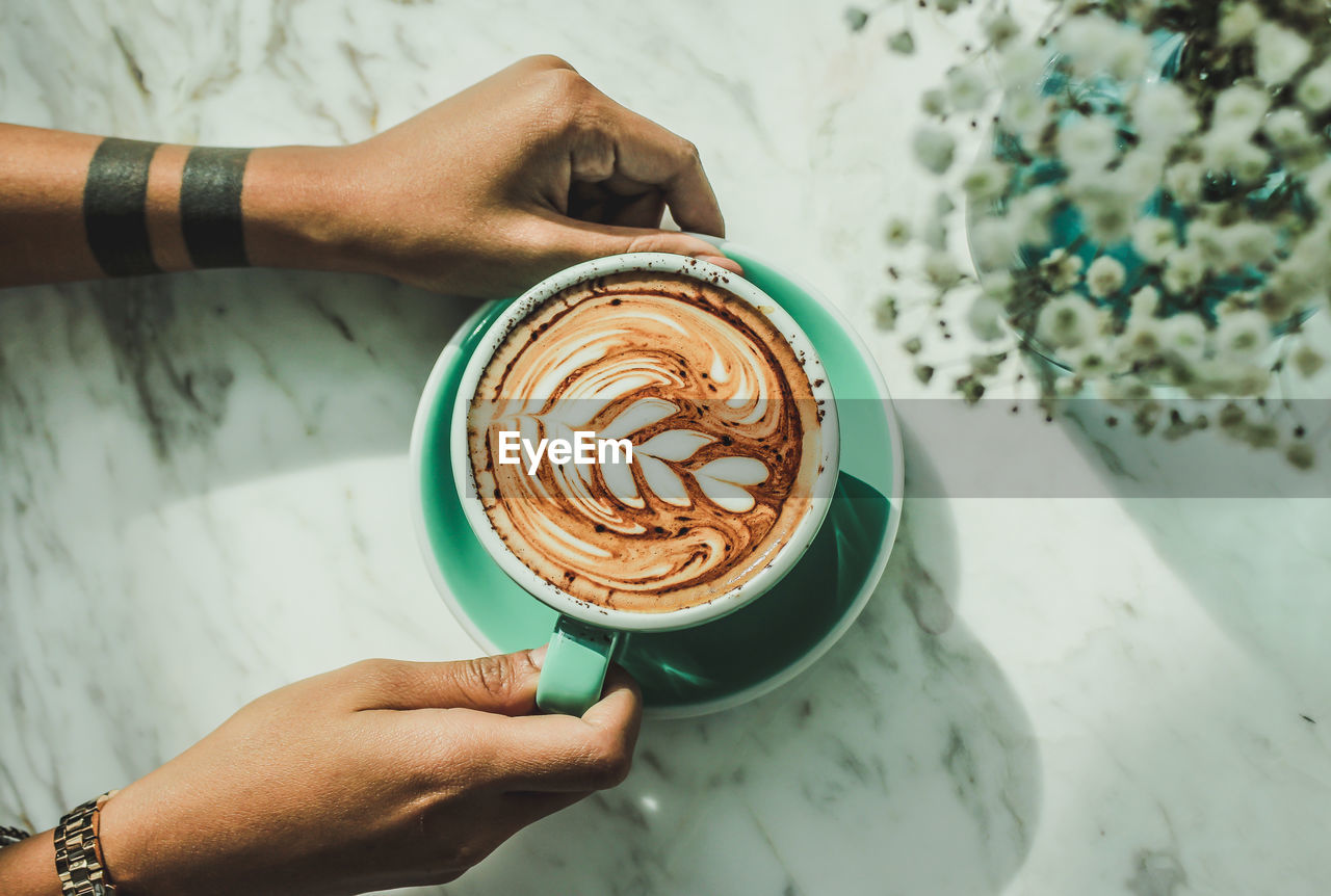 Cropped hands of man holding coffee cup on table