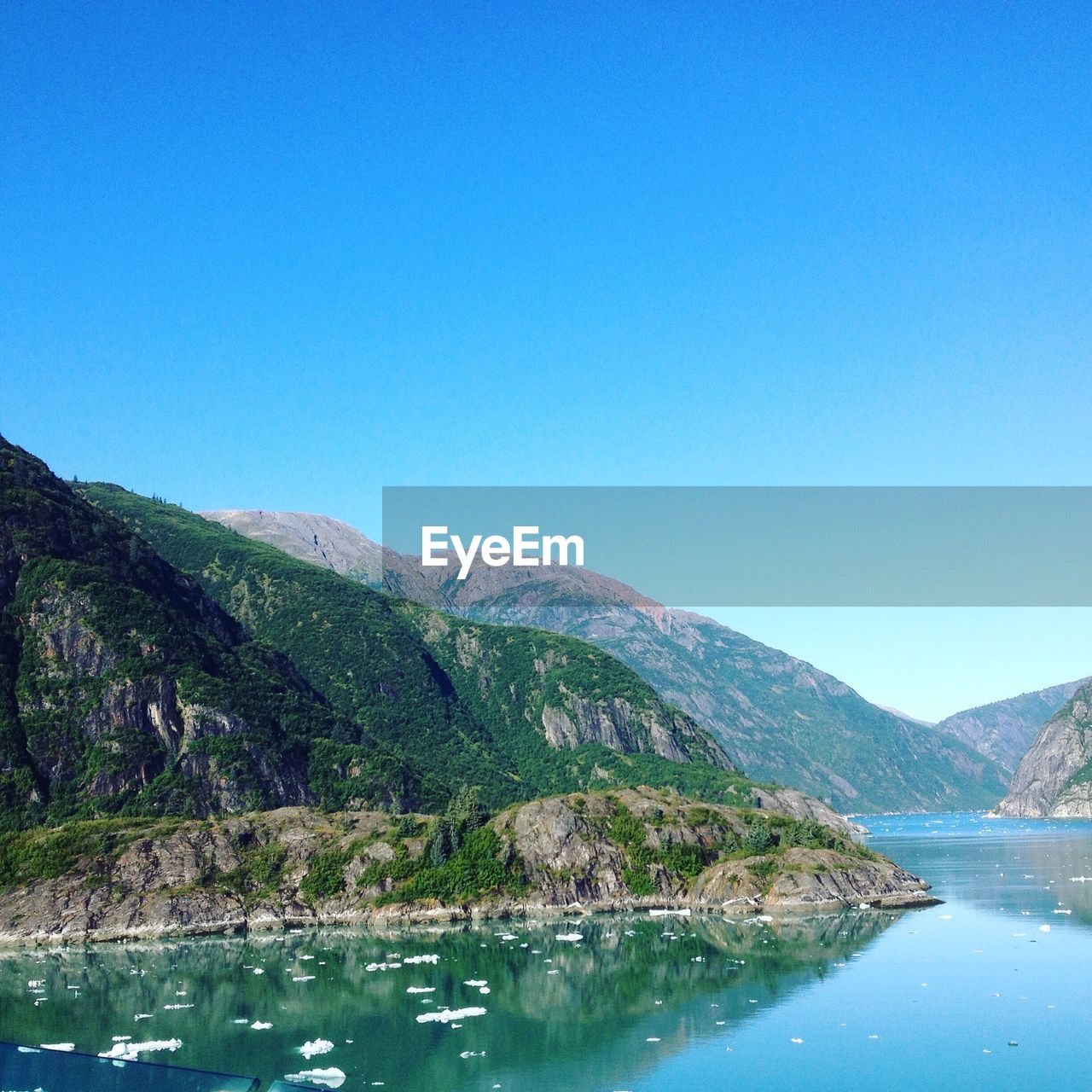 Scenic view of lake and mountains against clear blue sky