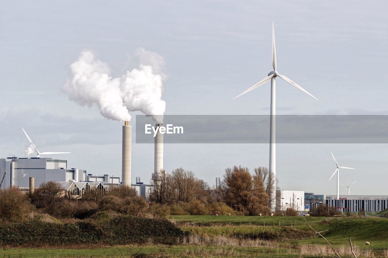 Windmill and industry against sky