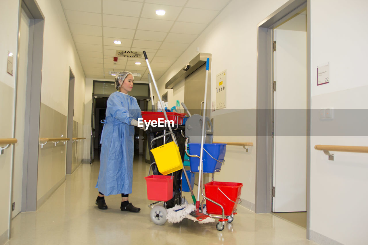 Full length of female cleaner working at corridor in hospital