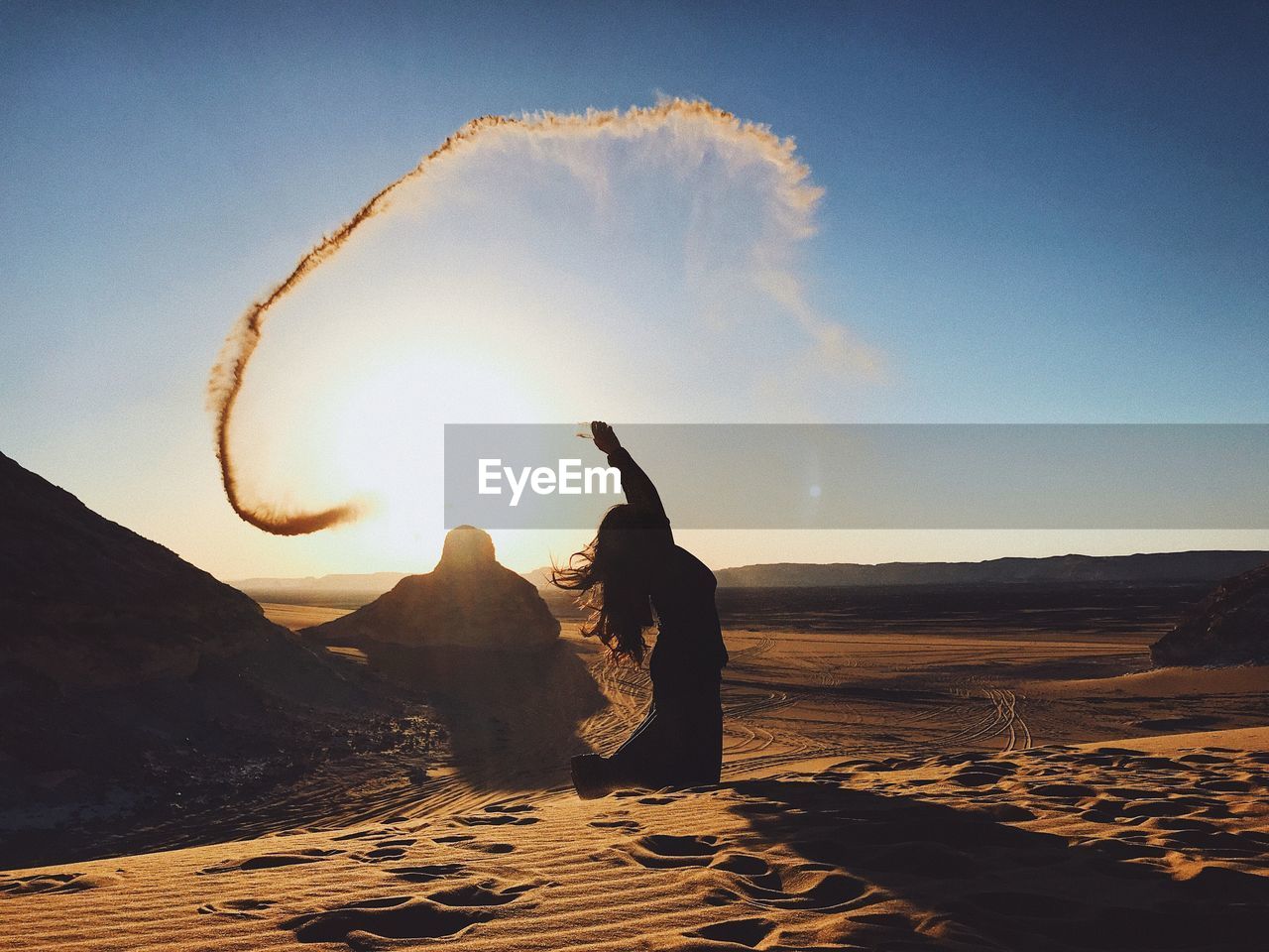 Woman throwing sand at desert against sky