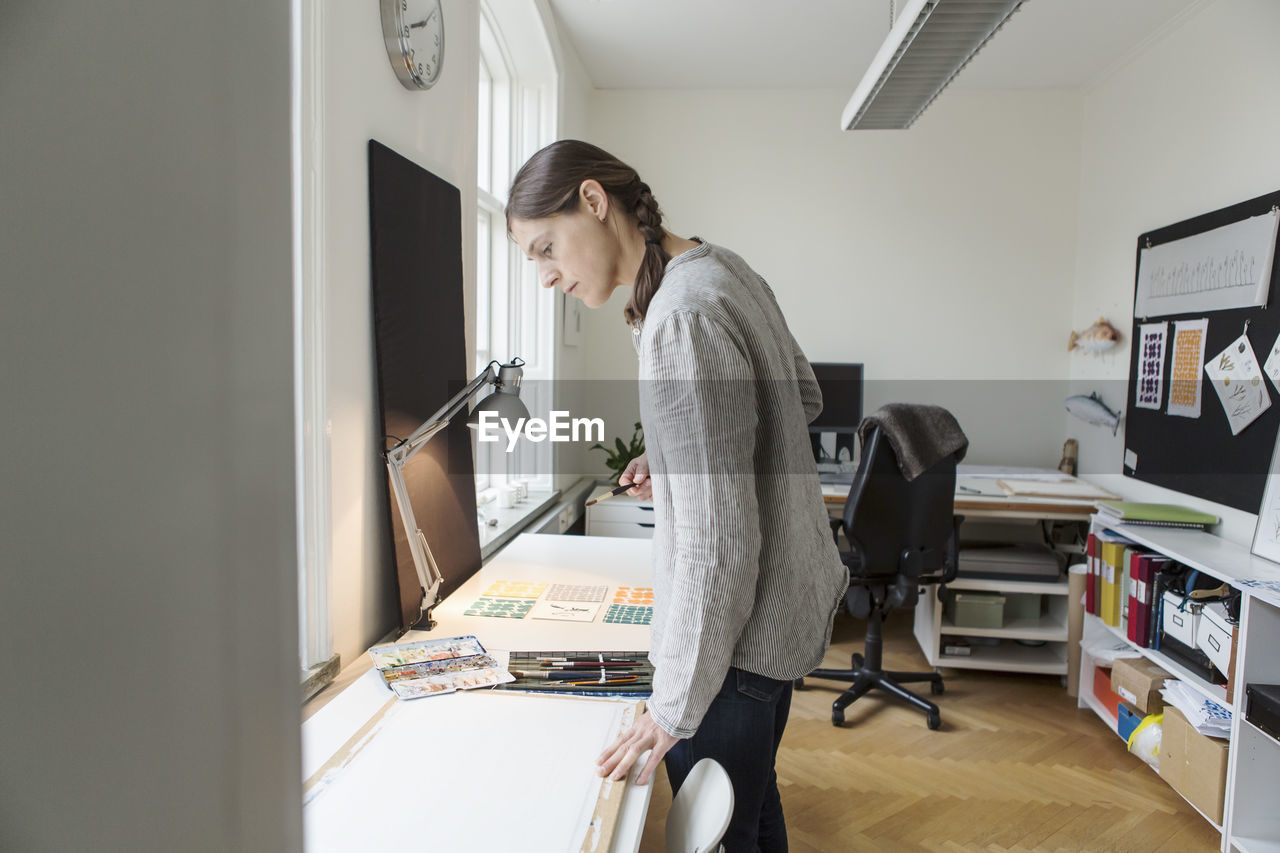 Serious woman looking at canvas while standing in creative office