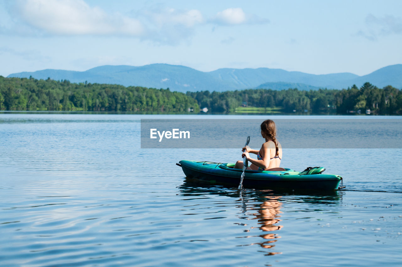 REAR VIEW OF WOMAN IN BOAT ON LAKE