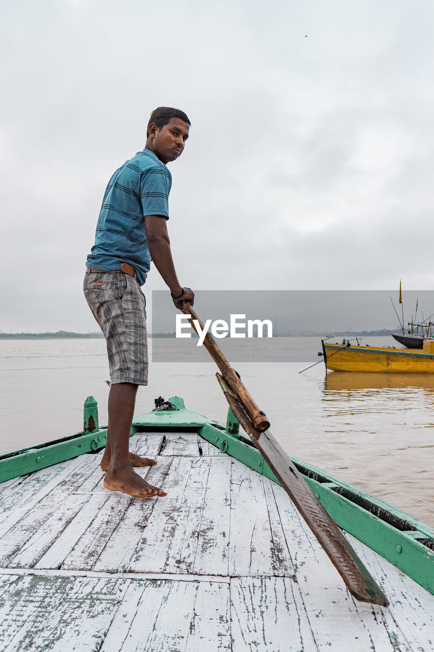 SIDE VIEW OF MAN STANDING ON WOODEN POST AGAINST SKY