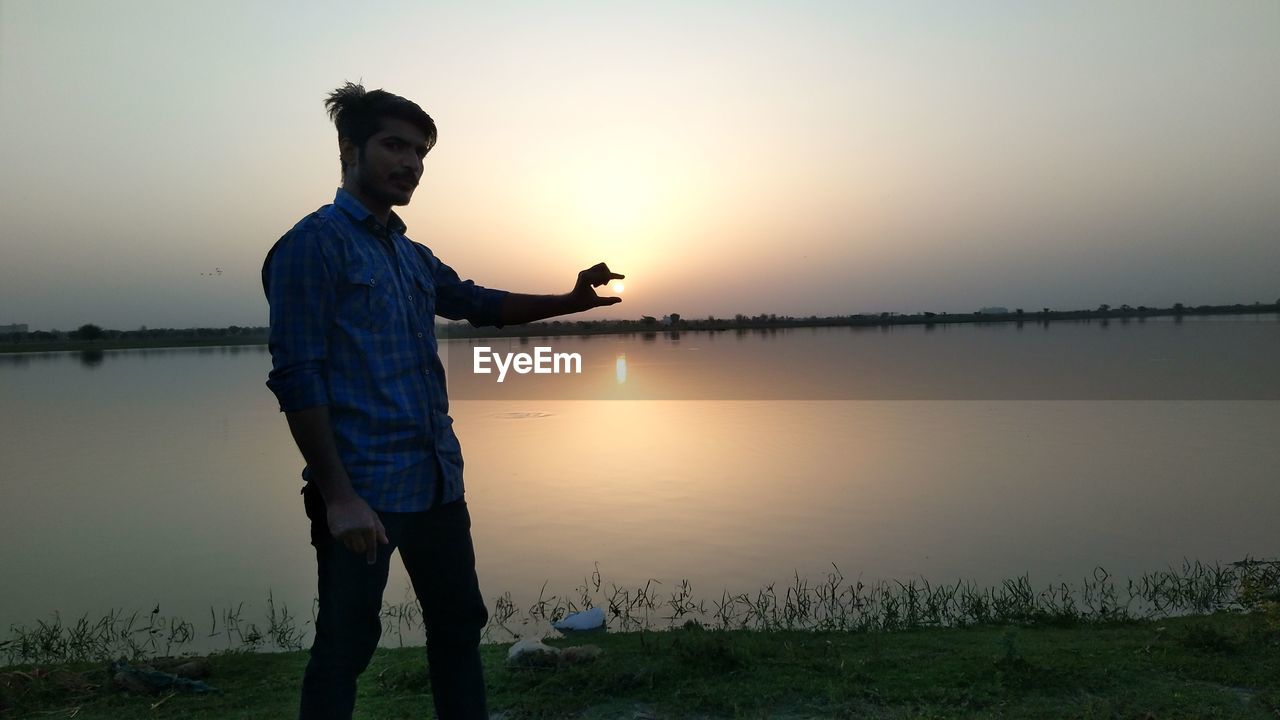 MAN STANDING AT LAKE DURING SUNSET