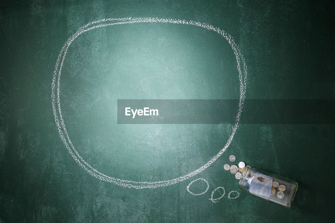 Directly above shot of blank speech bubble with currency in jar on blackboard