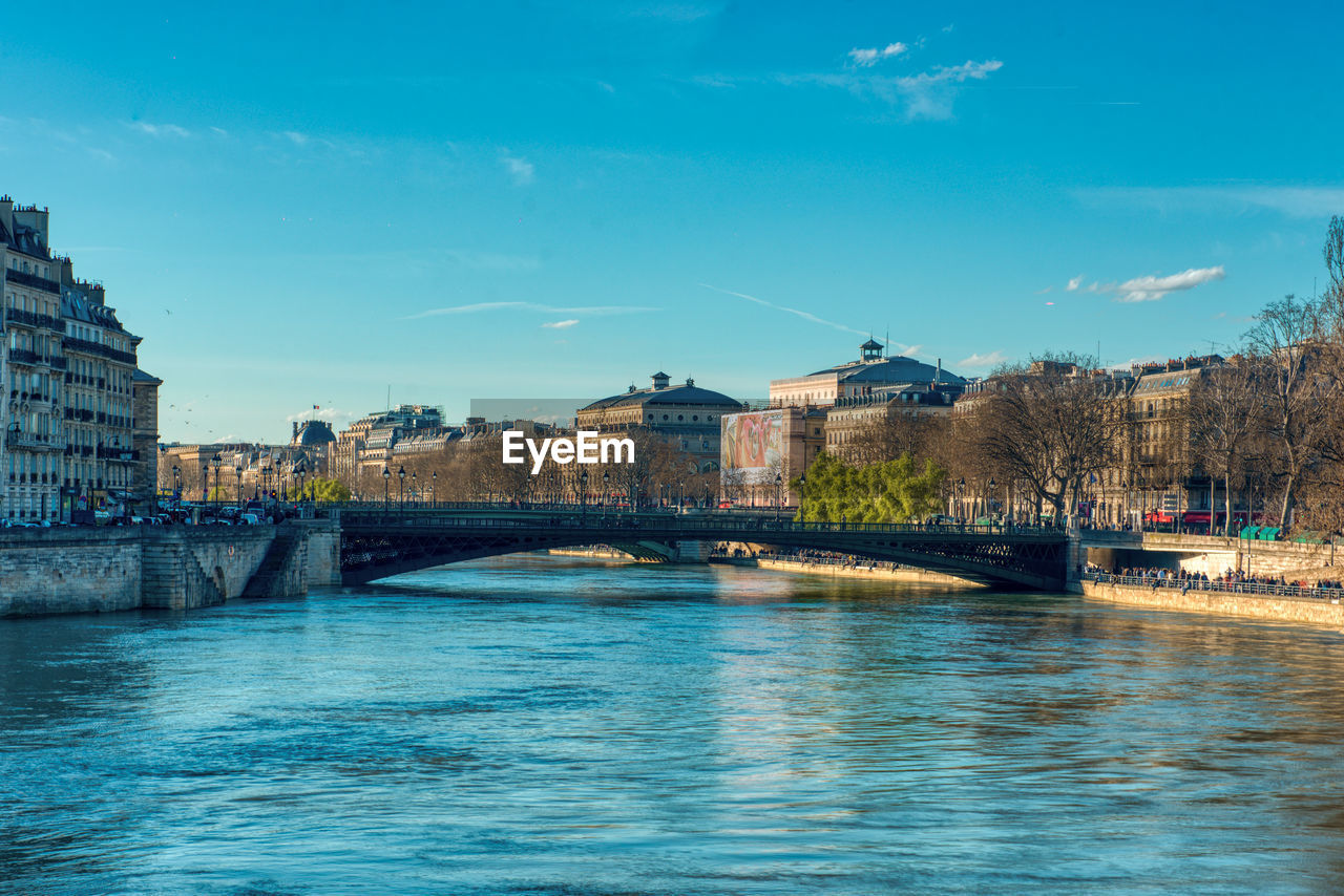 Bridge over river by buildings against blue sky