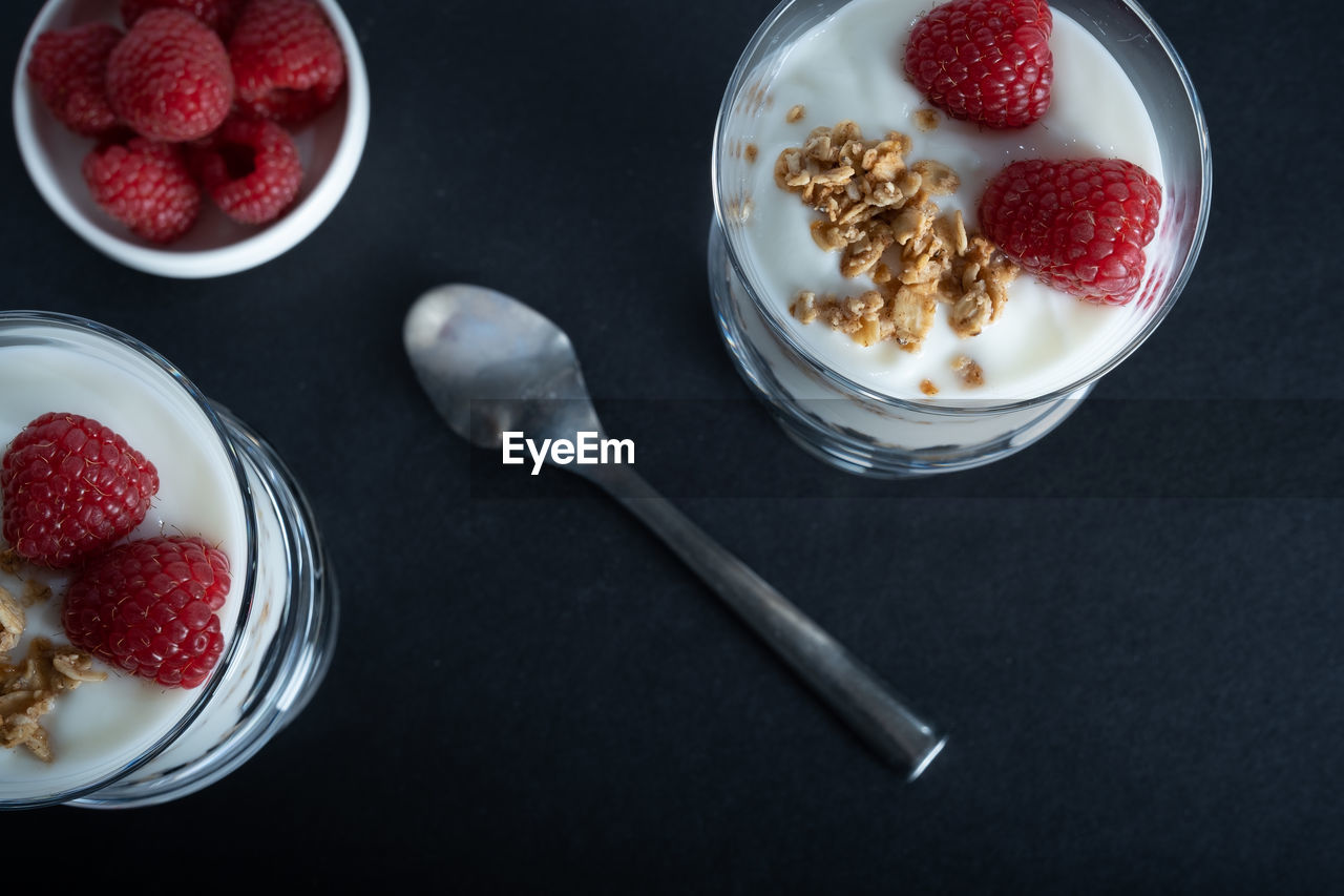 Two glass bowls of vanilla yogurt with cinnamon roll granola and raspberry topping