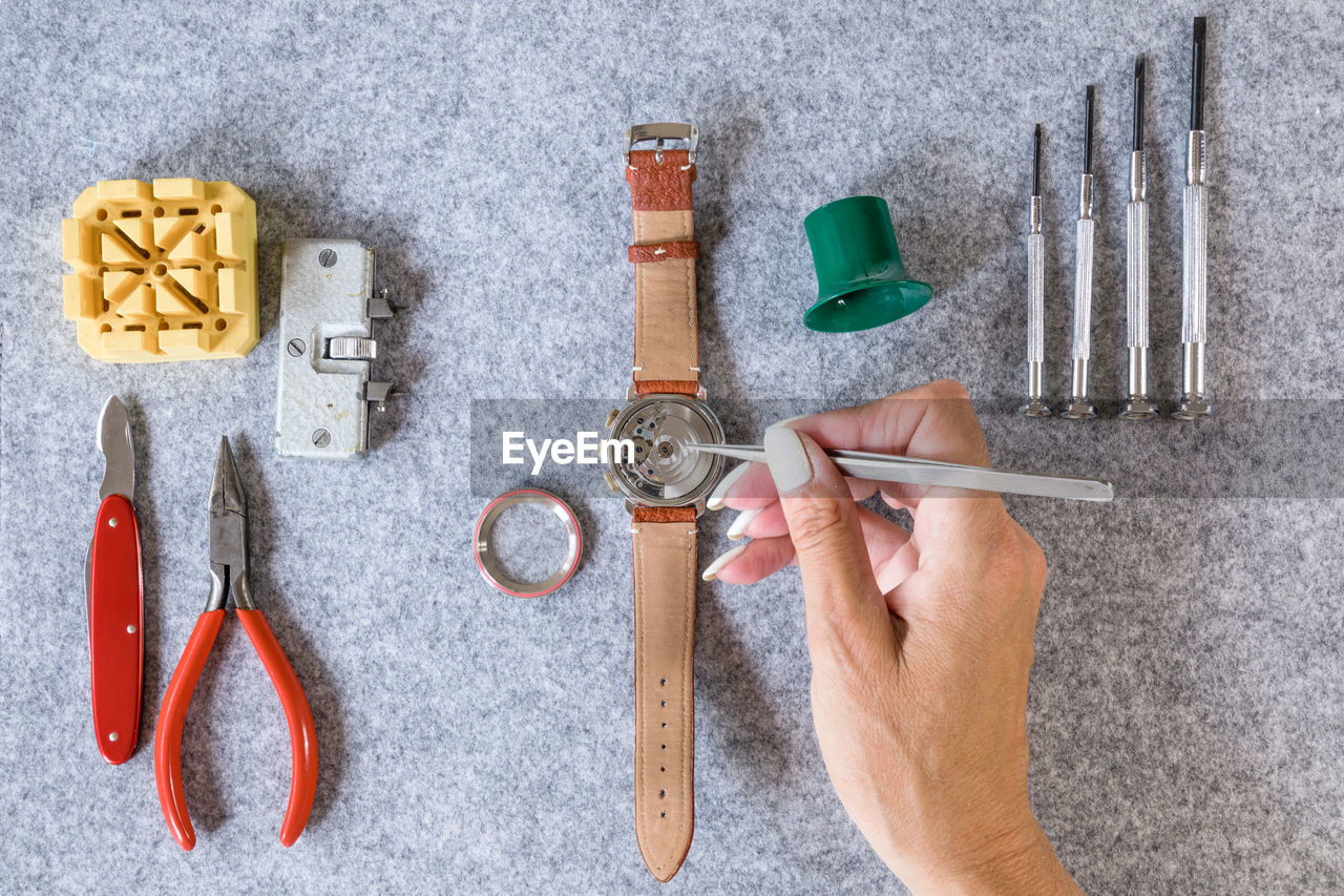 Cropped hand of woman repairing wristwatch with tools on table