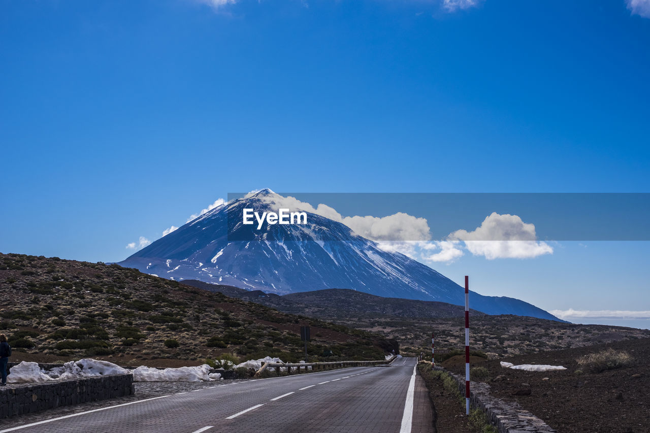 Road leading towards snowcapped mountains against blue sky