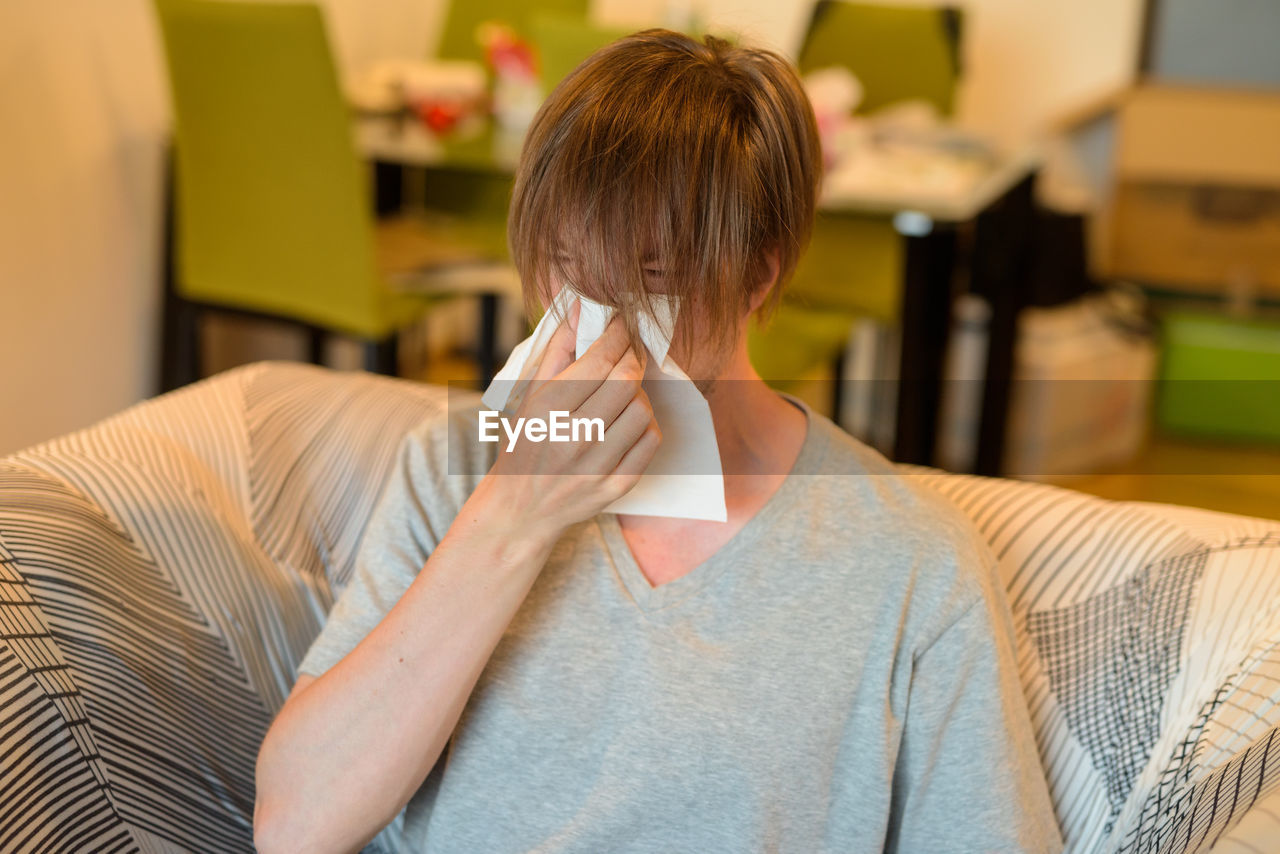 Man sneezing while sitting on sofa at home