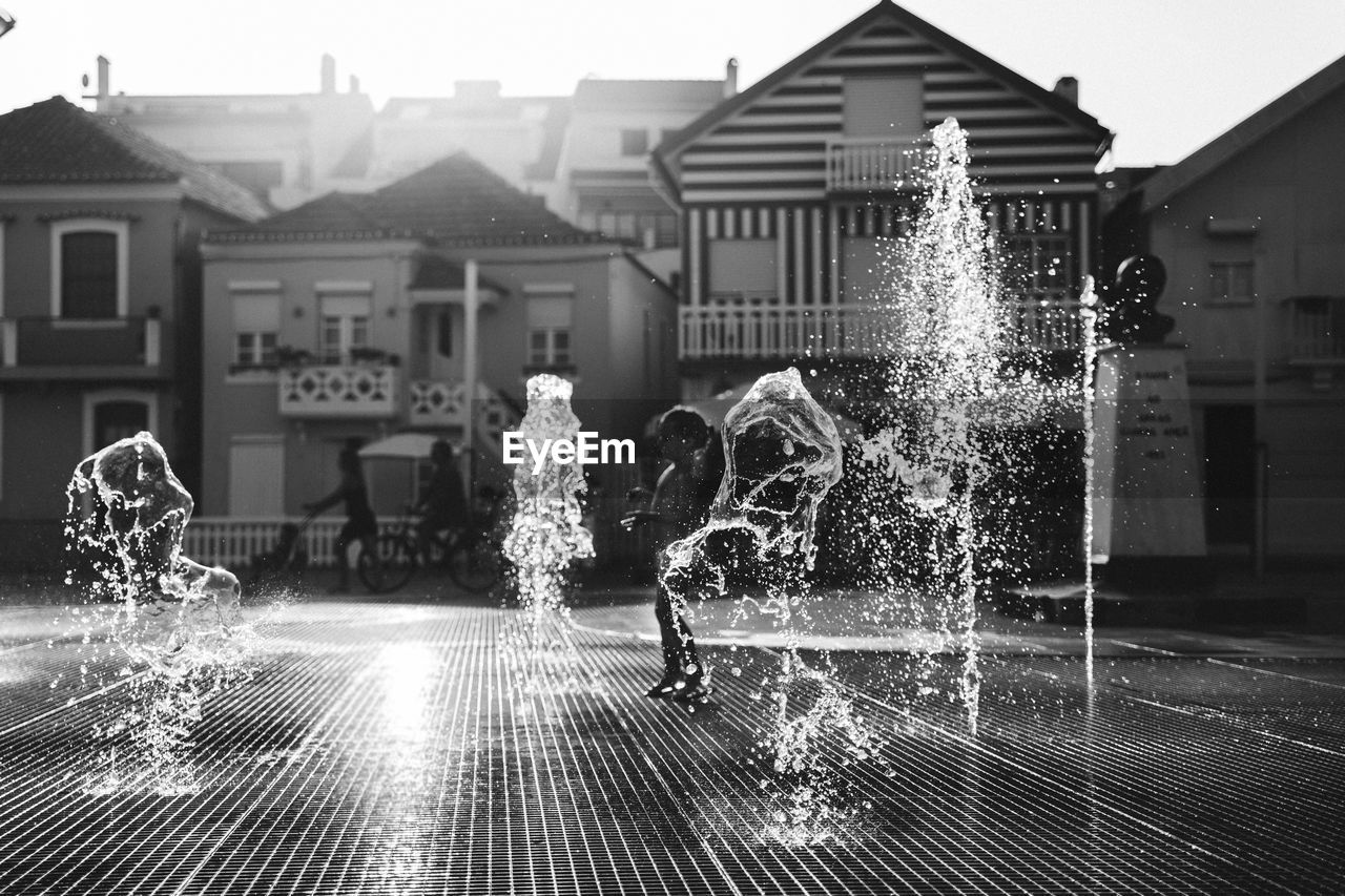 FULL LENGTH OF BOY SPLASHING WATER AGAINST HOUSES