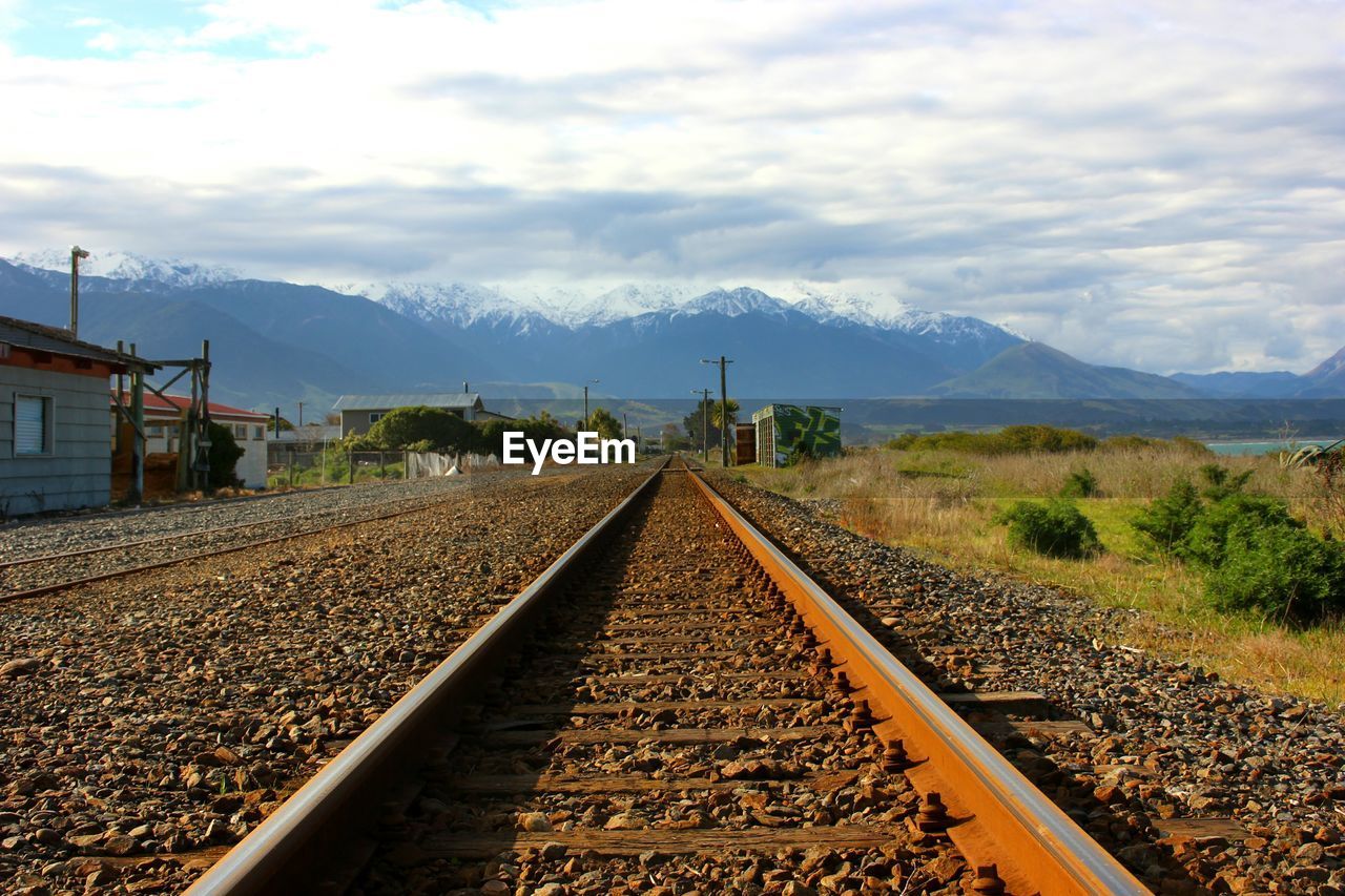 Railroad track and snowcapped mountains against cloudy sky