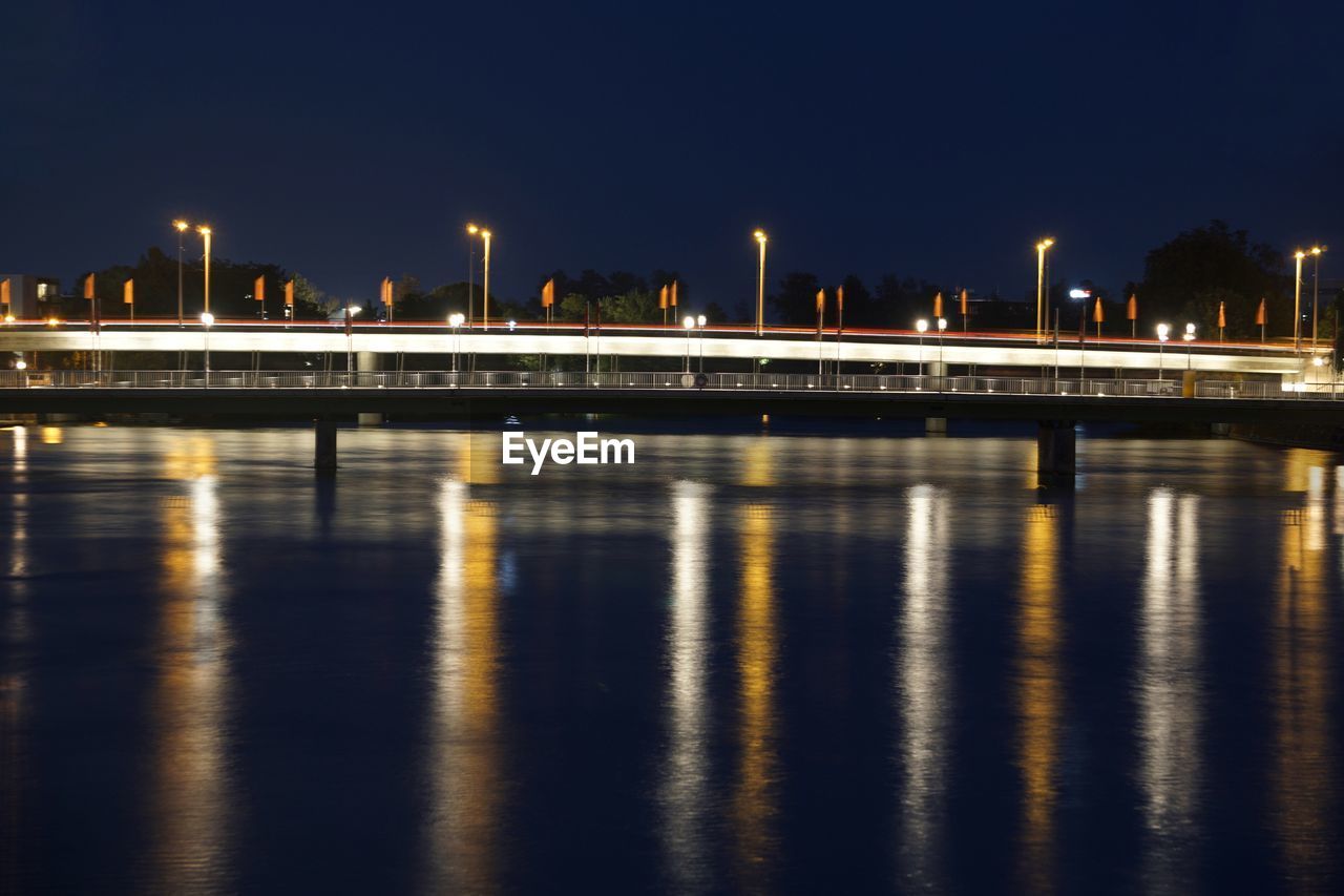 Illuminated buildings by river against sky at night