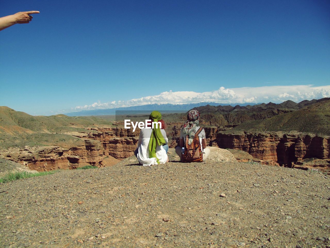 Rear view of women sitting on mountain against sky