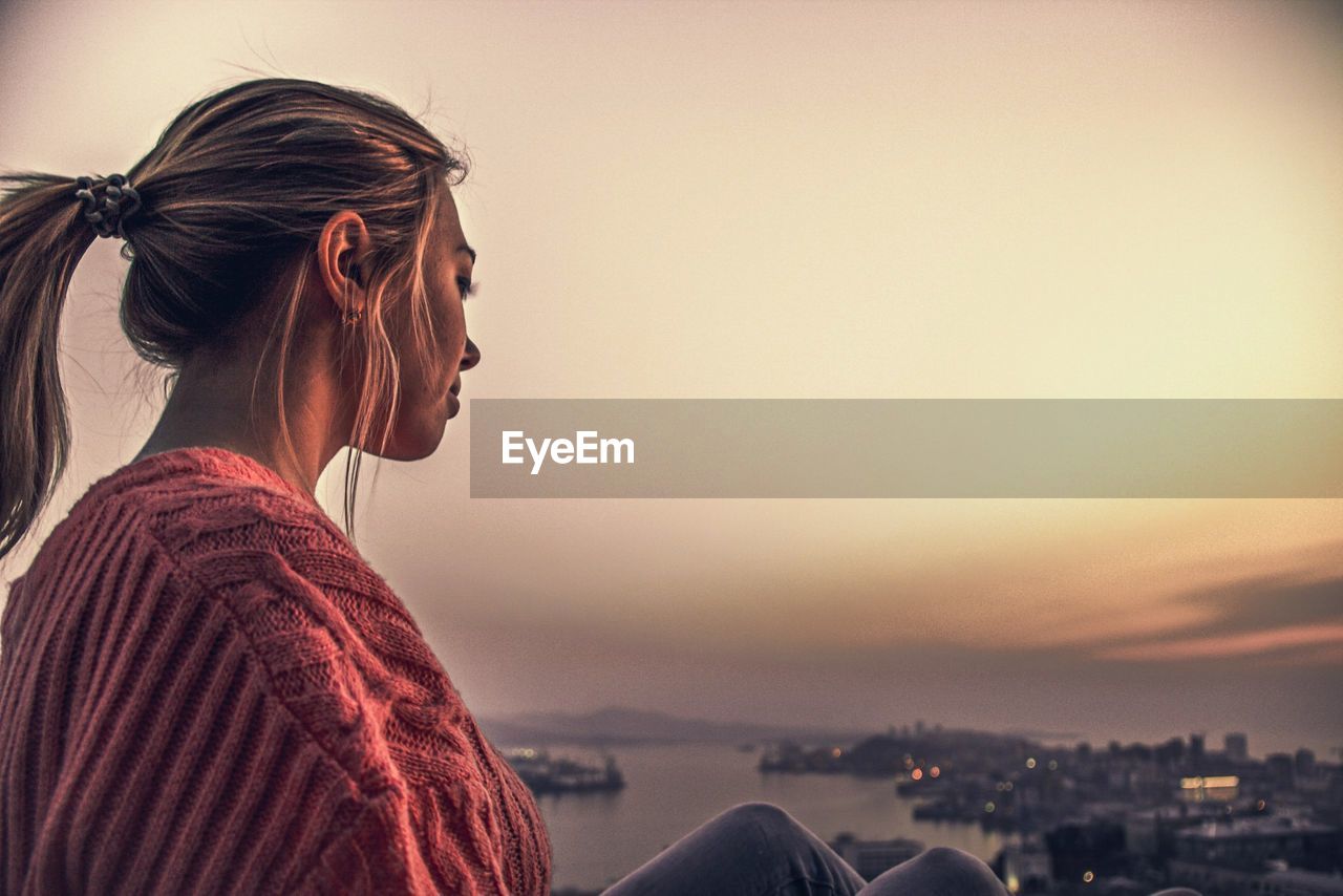 Side view of woman looking at cityscape against sky