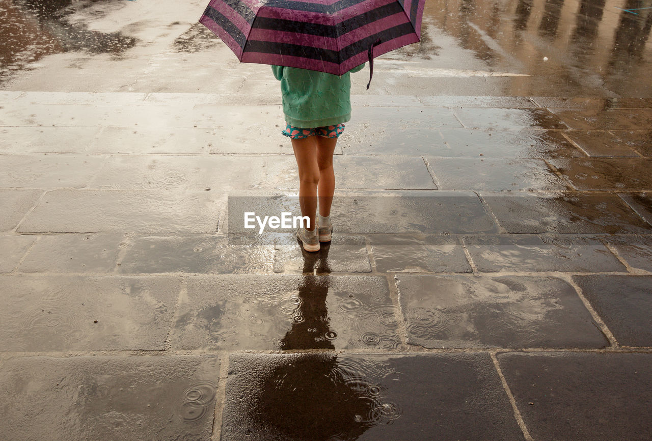 Low section of woman standing on wet footpath