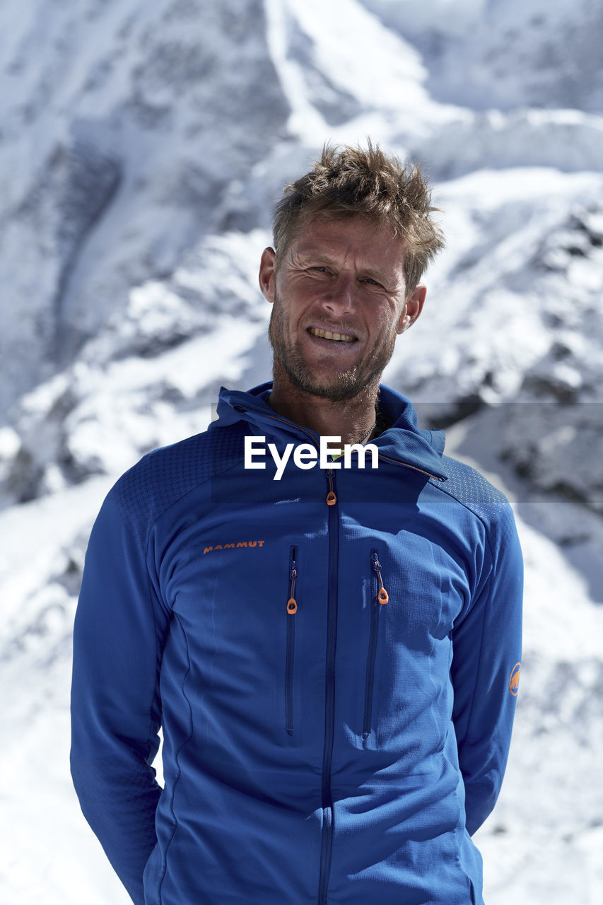 Portrait of mature man smiling while standing against snowcapped mountains