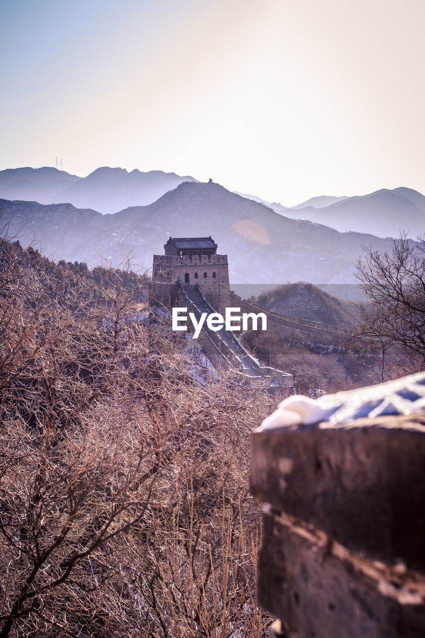 View of tower and great wall of china mountain range against sky with mist across the mountains