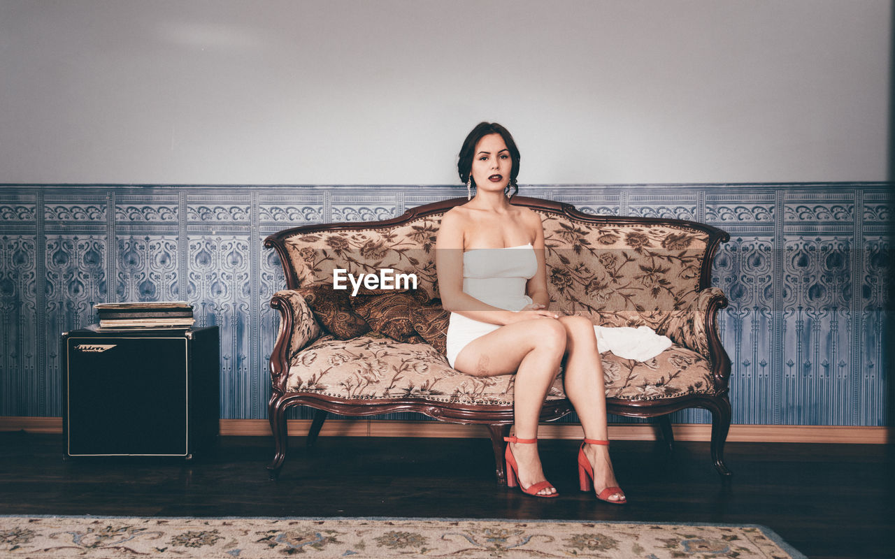 Full length of fashionable young woman sitting on chair against wall