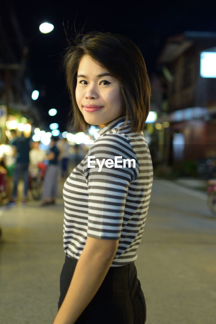 Portrait of smiling beautiful young woman standing on street in city