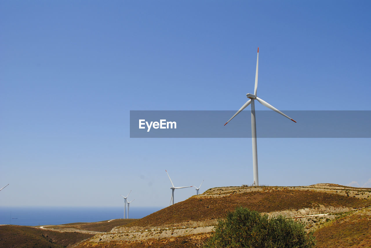 Windmills on field against clear blue sky